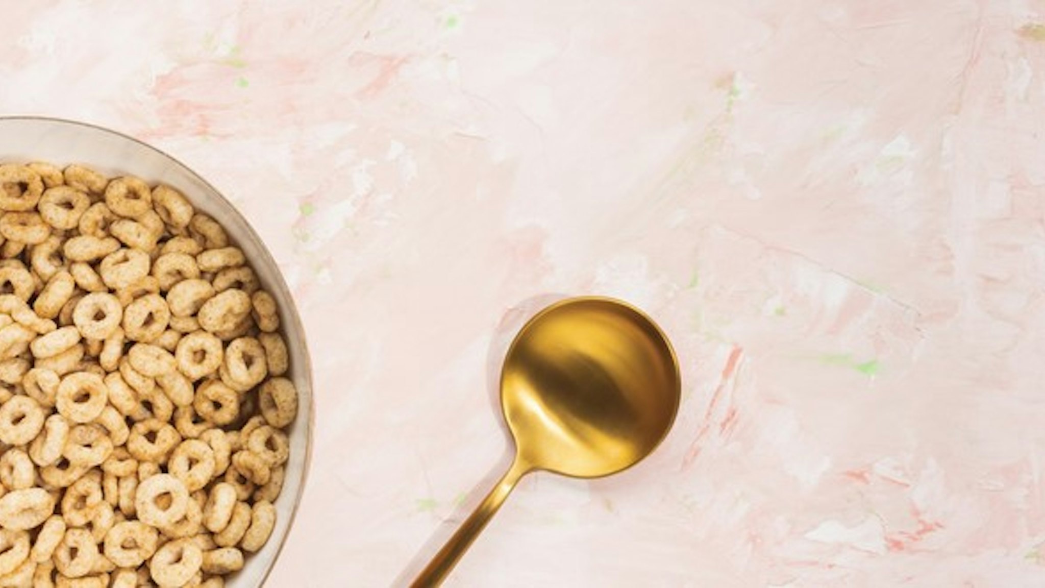 Delicious honey cheerios cereal in a bowl and golden spoon on pink background. Top view, copy space