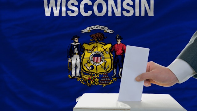 man putting ballot in a box during elections in front of flag american state of wisconsin