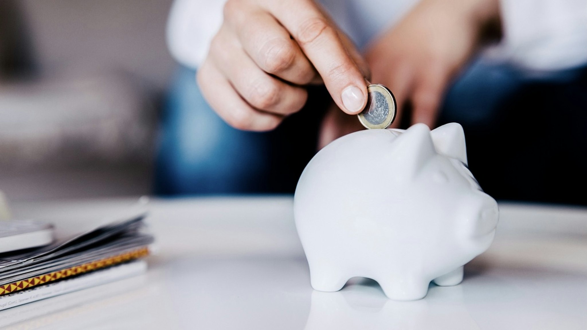 Putting a coin in a white piggy bank at home. - stock photo Putting a coin in a white piggy bank at home. Guido Mieth via Getty Images