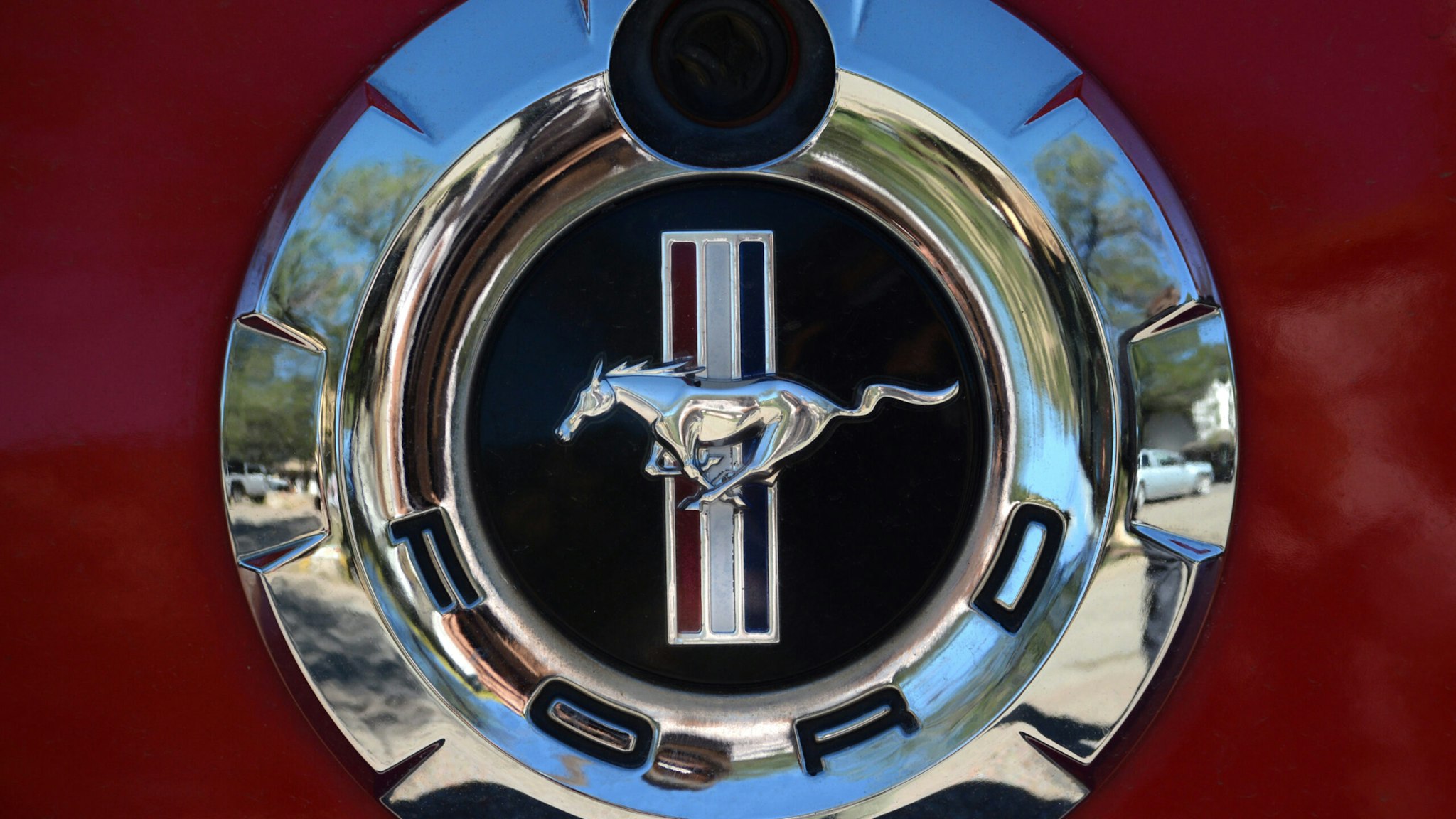 A Ford Mustage logo and emblem and rear-view or backup camera lens on a red Mustang parked in Santa Fe, New Mexico.