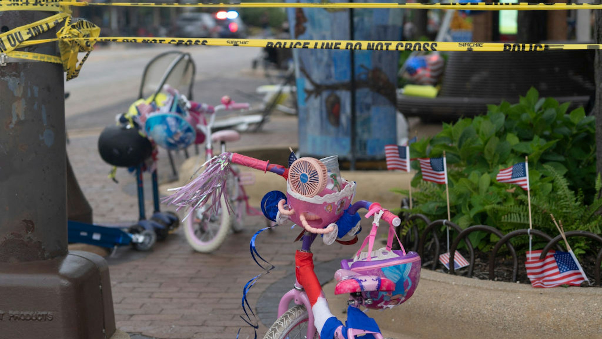 Police crime tape is seen around the area where children's bicycles and baby strollers stand near the scene of the Fourth of July parade shooting in Highland Park, Illinois on July 4, 2022. - A shooter opened fire Monday during a parade to mark US Independence Day in the state of Illinois, killing at least six people, officials said. "At this time, two dozen people have been transported to Highland Park hospital. Six are confirmed deceased," Commander Chris O'Neil of the city's police told journalists. The suspected shooter, who is still at large, has been described as a white male aged 18-20 with longer black hair, O'Neil said. (Photo by Youngrae Kim / AFP) (Photo by YOUNGRAE KIM/AFP via Getty Images)
