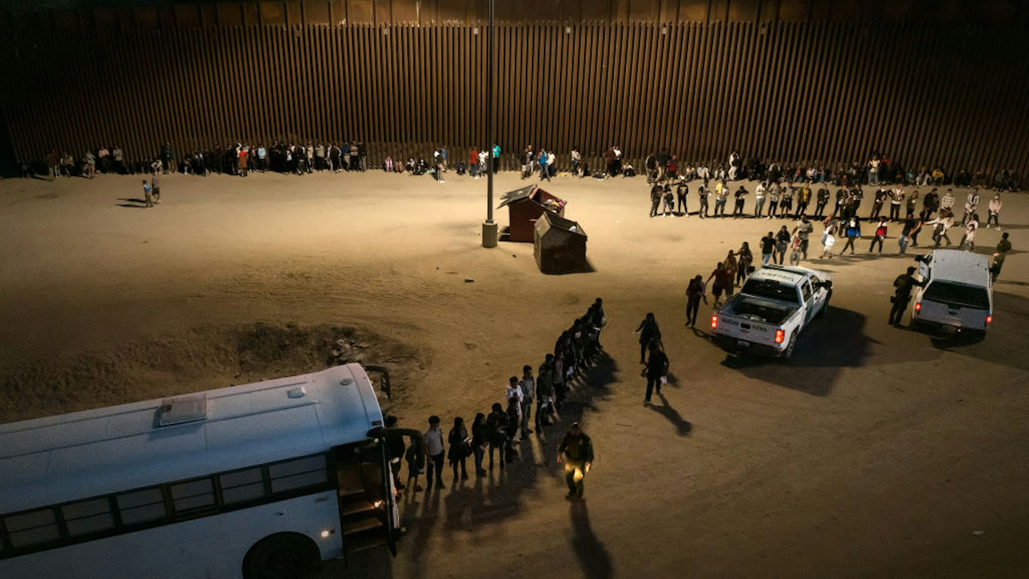 Aerial view of immigrants entering a Border Patrol vehicle to be taken for processing, after crossing the border from Mexico on June 23, 2022 in Yuma, Arizona.