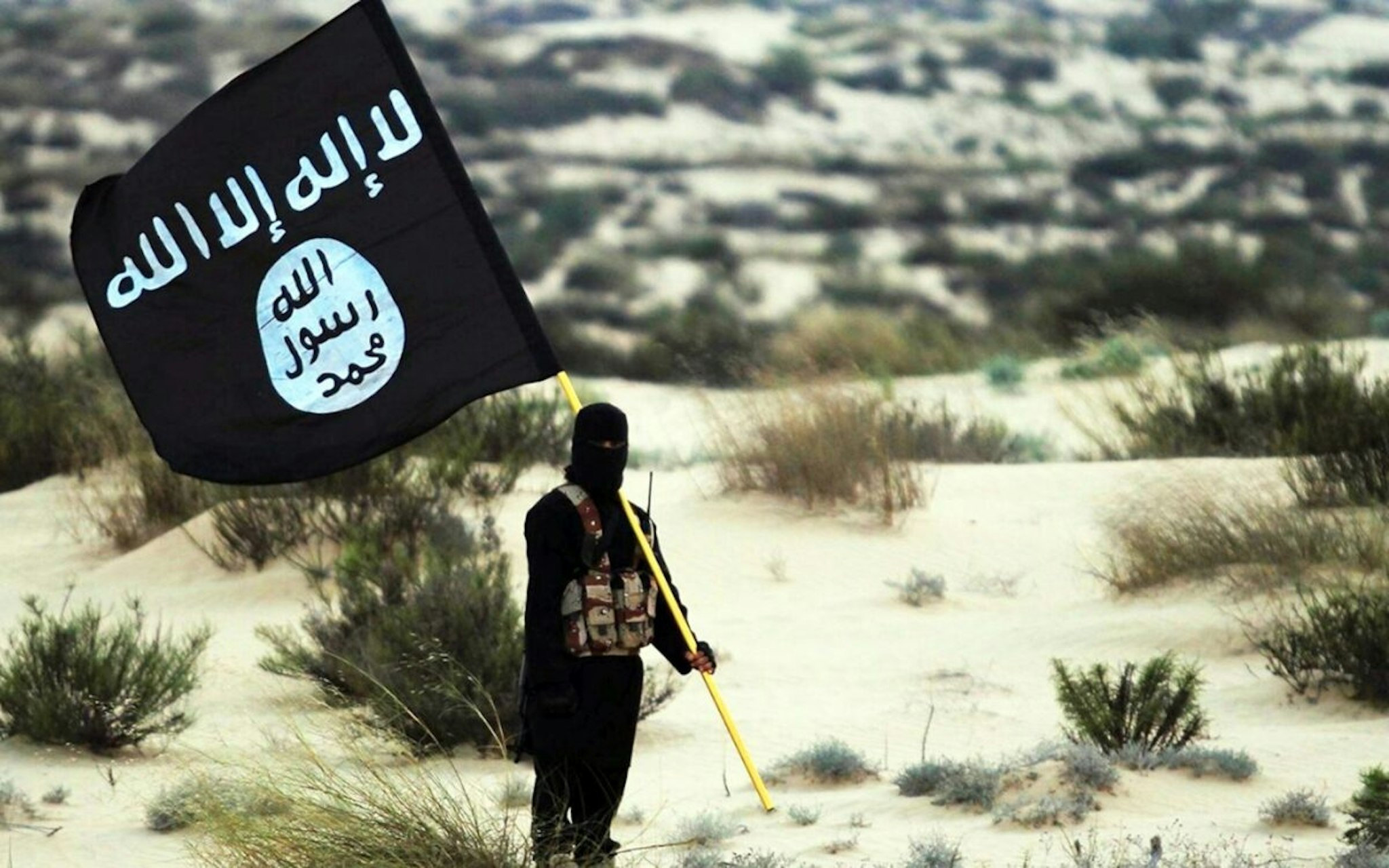 Islamic State/Iraq/Syria: A masked Islamic State soldier poses holding the ISIL banner somewhere in the deserts of Iraq or Syria