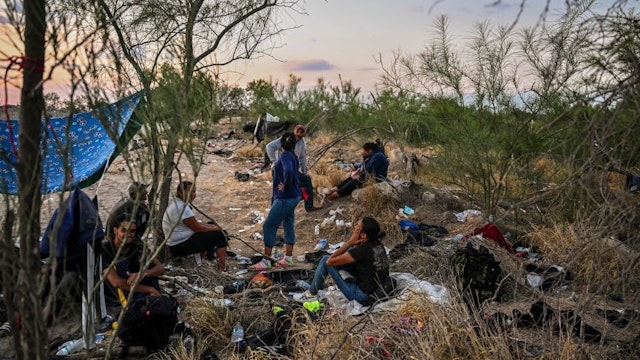 Migrants rest after crossing the Rio Grande River as they wait to get apprehended by Border Patrol agents as National Guard agents sit on a car across the street (out of frame), in Eagle Pass, Texas, at the border with Mexico on June 30, 2022. - Every year, tens of thousands of migrants fleeing violence or poverty in Central and South America attempt to cross the border into the United States in pursuit of the American dream. Many never make it. On June 27, around 53 migrants were found dead in and around a truck abandoned in sweltering heat near the Texas city of San Antonio, in one of the worst disasters on the illegal migrant trail. (Photo by CHANDAN KHANNA / AFP) (Photo by CHANDAN KHANNA/AFP via Getty Images)