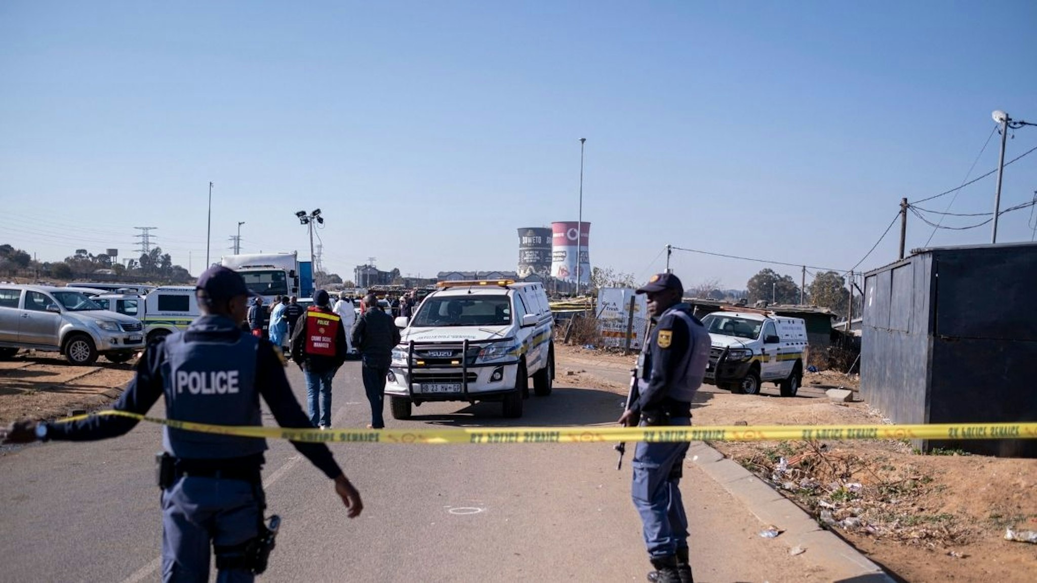 South African Police Service (SAPS) officers enforce a perimeter around a crime scene as pathalogical investigators inspect the crime scene where 14 people where shot dead in a tavern as a forensic team investigates in Soweto on July 10, 2022.