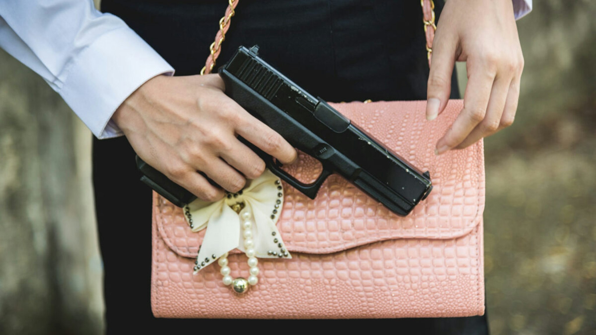 Midsection Of Woman With Shoulder Bag Holding Gun