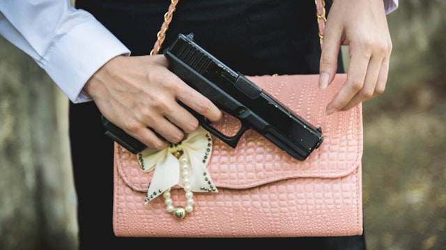 Midsection Of Woman With Shoulder Bag Holding Gun