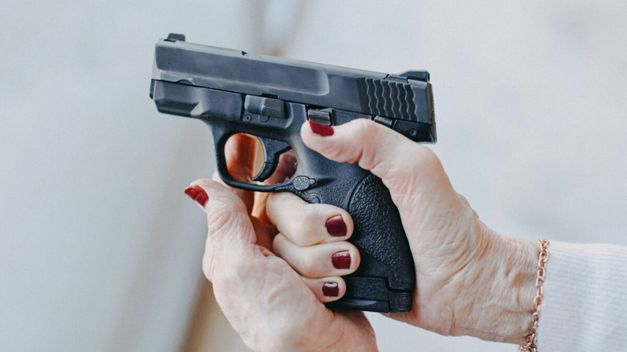 Senior woman's hands holding a pistol.