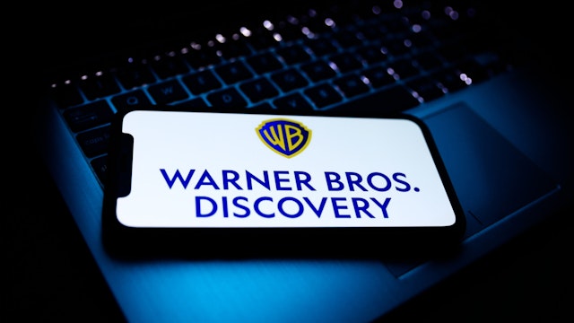 Warner Bros. Discovery logo displayed on a phone screen and a laptop keyboard are seen in this illustration photo taken in Krakow, Poland on April 9, 2022.