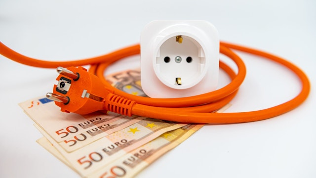 Euro banknotes under a power cable. Expensive concepts of energy and cost of electricity. Front view. Electric power cable with plug and socket unplugged