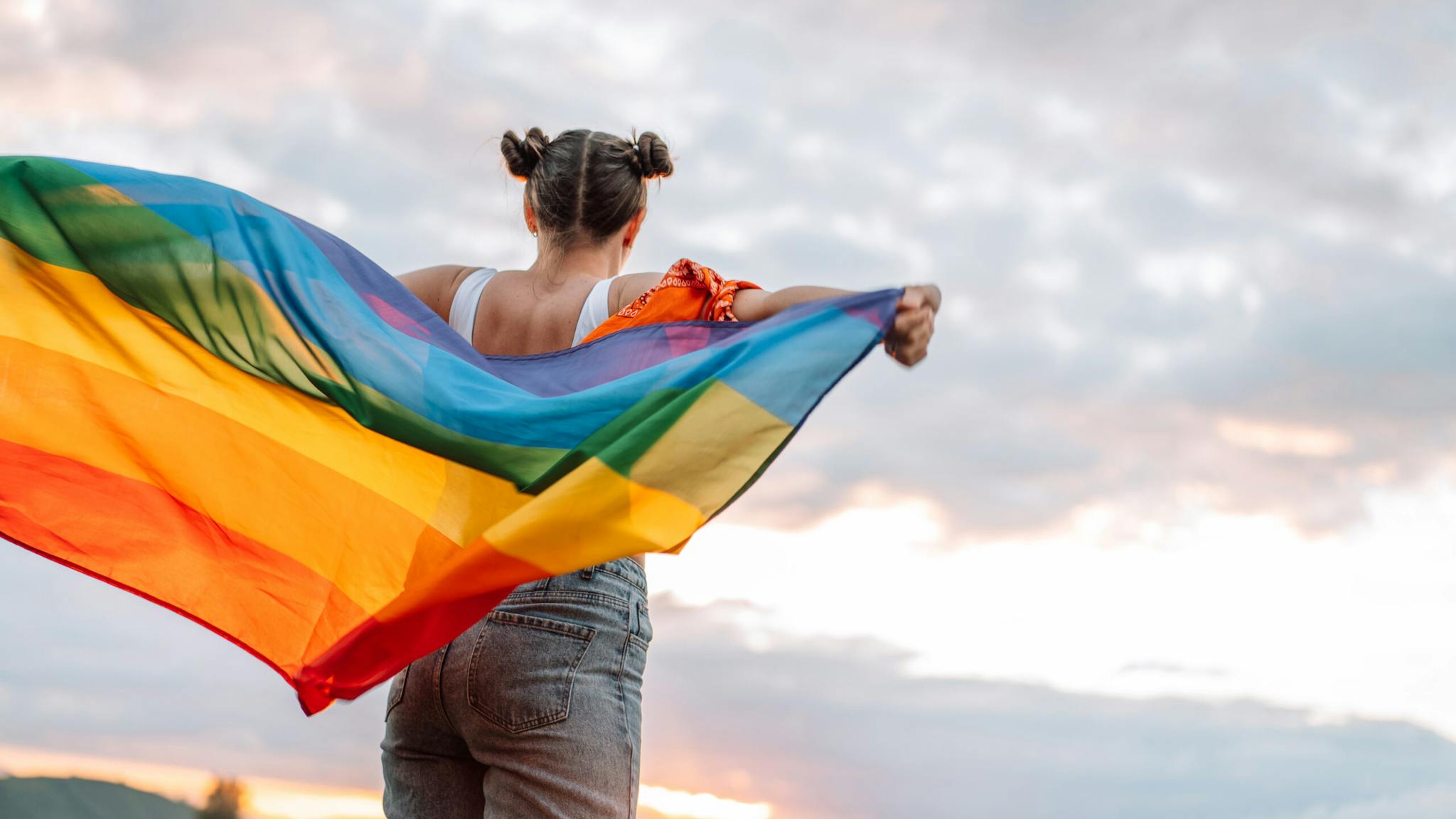 diversity Girl standing back and holding rainbow flag on sky background