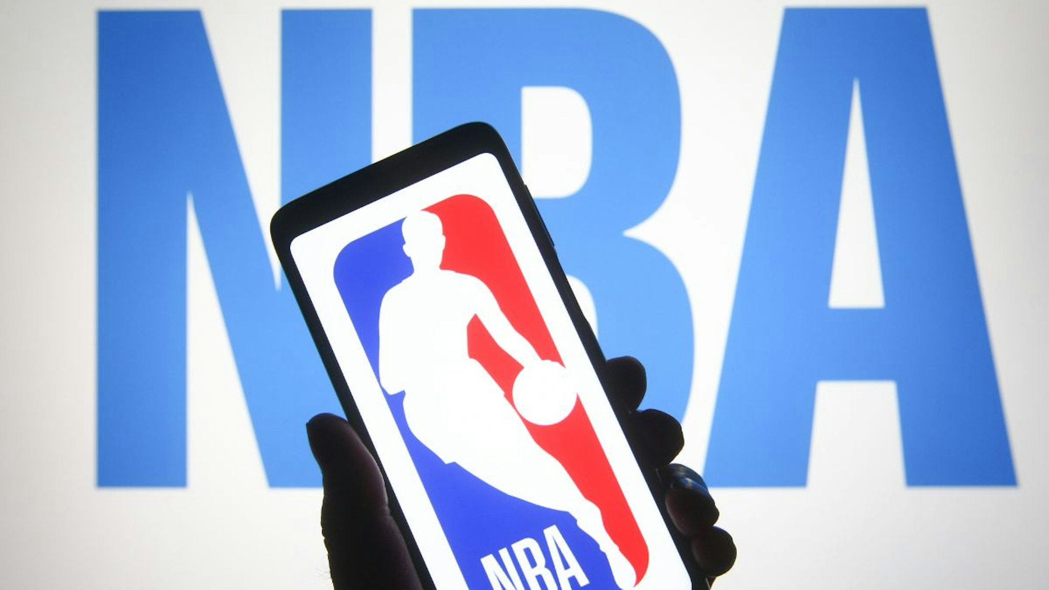In this photo illustration a National Basketball Association (NBA) logo is seen on a smartphone and a pc screen.