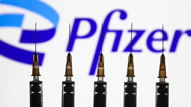 Medical syringes and Pfizer logo displayed on a screen in the background are seen in this illustration photo taken in Krakow, Poland on January 26, 2022.