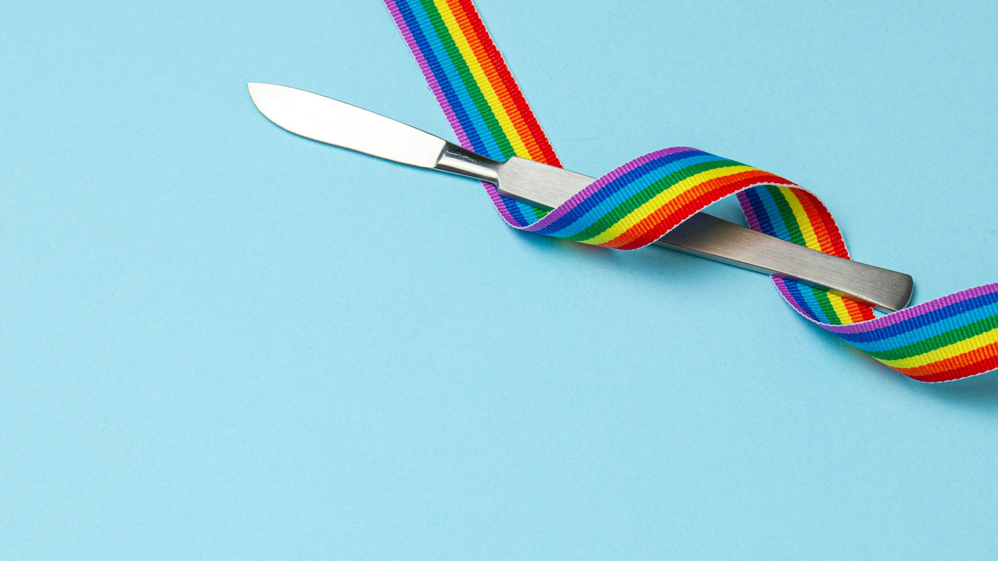 Scalpel and rainbow LGBT ribbon pride symbol. Sex change operation. Blue background. Copy space for text