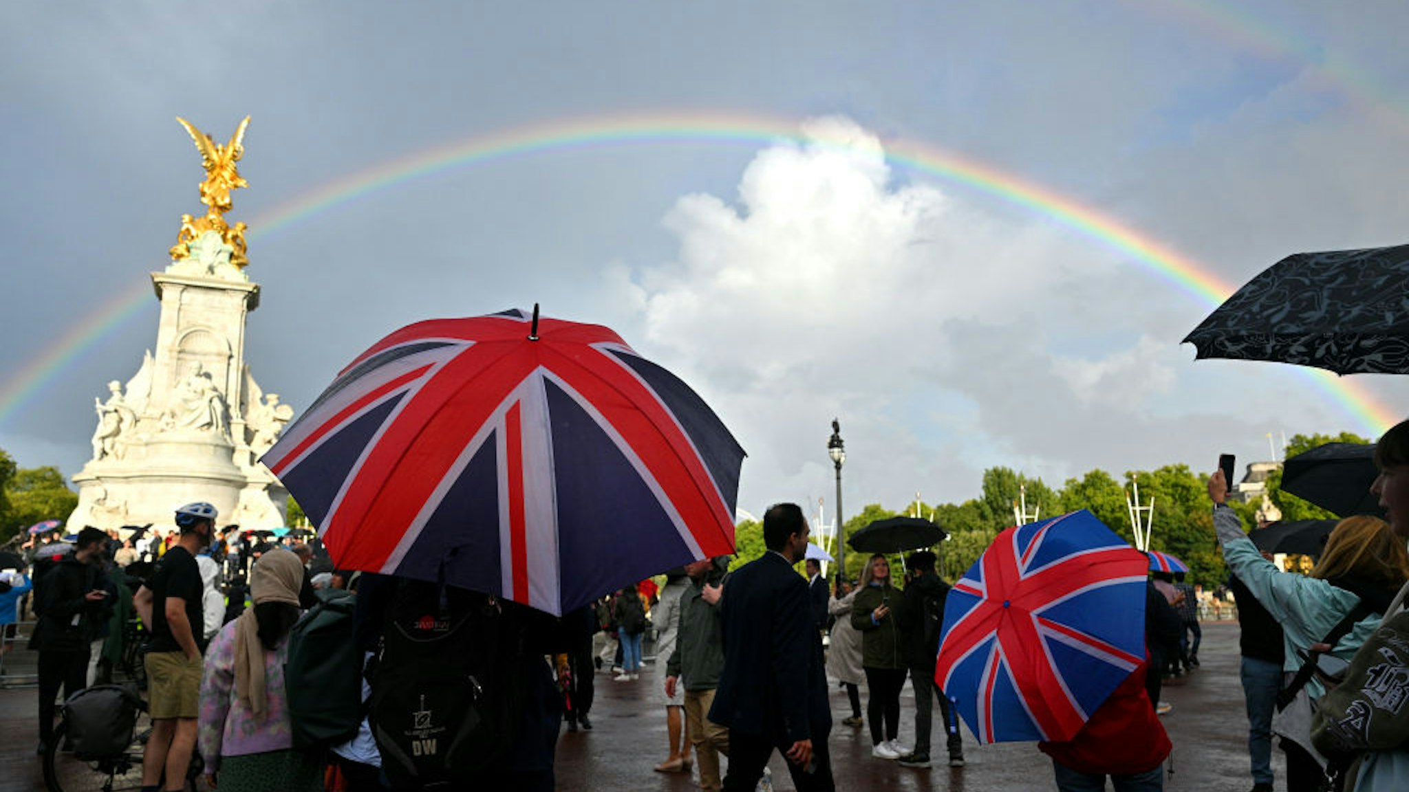 LONDON, ENGLAND - SEPTEMBER 08: A man looks on holding a Union flag umbrella as a rainbow is seen outside of Buckingham Palace on September 08, 2022 in London, England. Buckingham Palace issued a statement earlier today saying that Queen Elizabeth was placed under medical supervision due to concerns about her health.