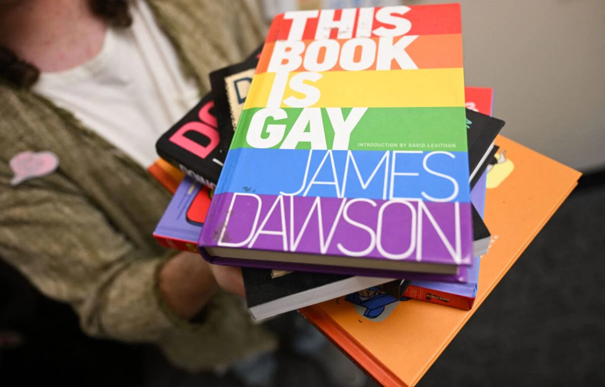 Laramie Pridefest Board Member, Tyler Wolfgang, displays a stack of books, some of which have been banned across the US due to controversy, including "This Book is Gay", in their office on the University of Wyoming campus in Laramie, Wyoming, on August 13, 2022