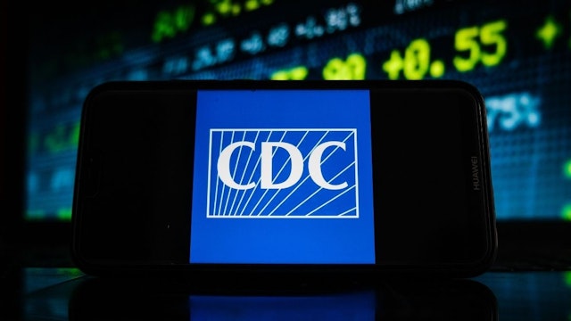 In this photo illustration a CDC logo seen displayed on a smartphone screen with stock market graphic on the background.