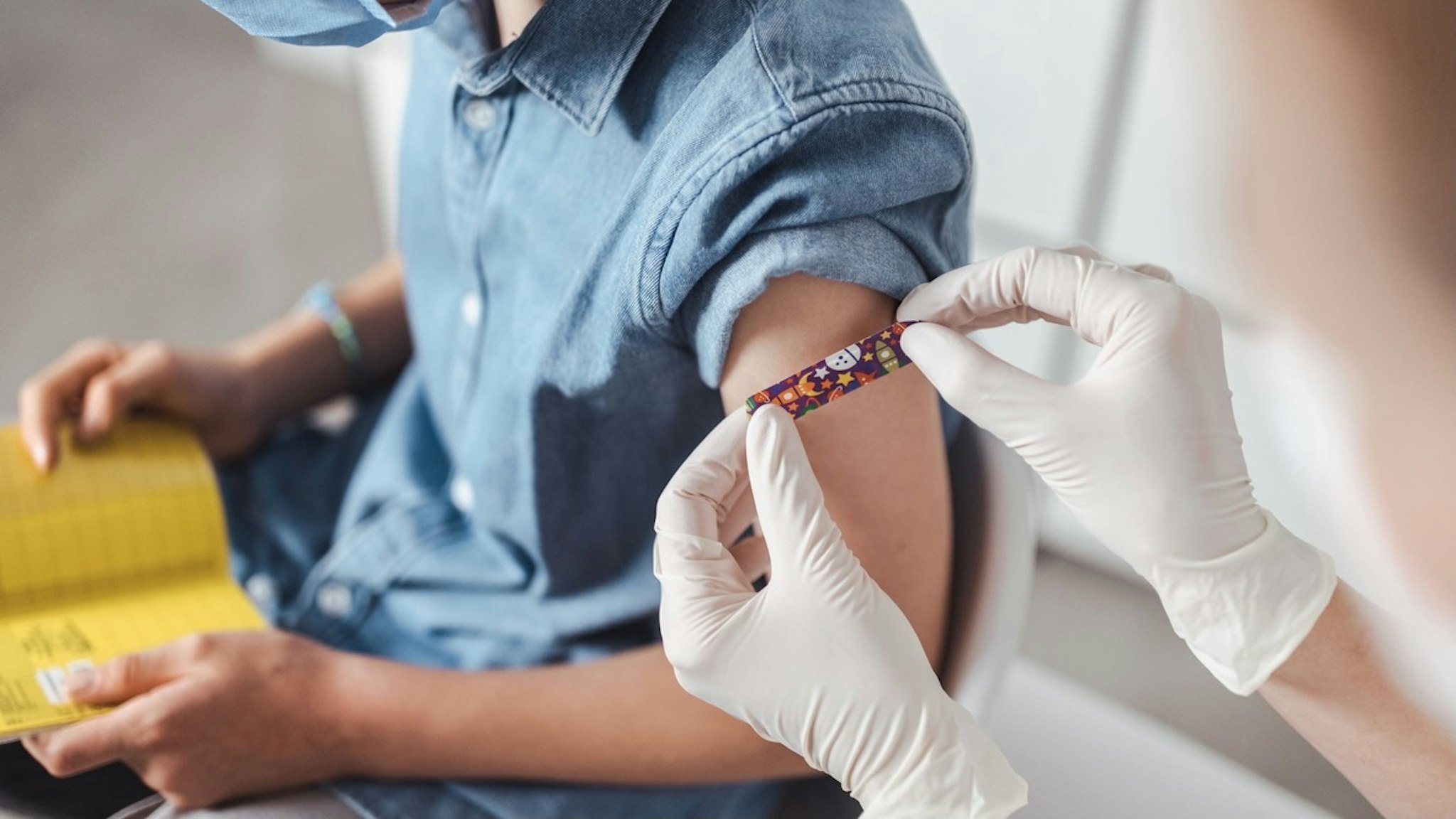 Nurse putting adhesive bandage on boy's arm at vaccination center - stock photo Westend61 via Getty Images