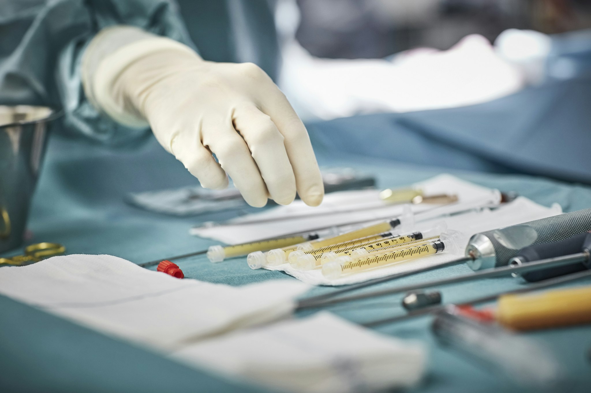 Cropped image of female surgeon reaching for syringes on table. Close-up of healthcare worker's hand wearing surgical glove. She is in emergency room.