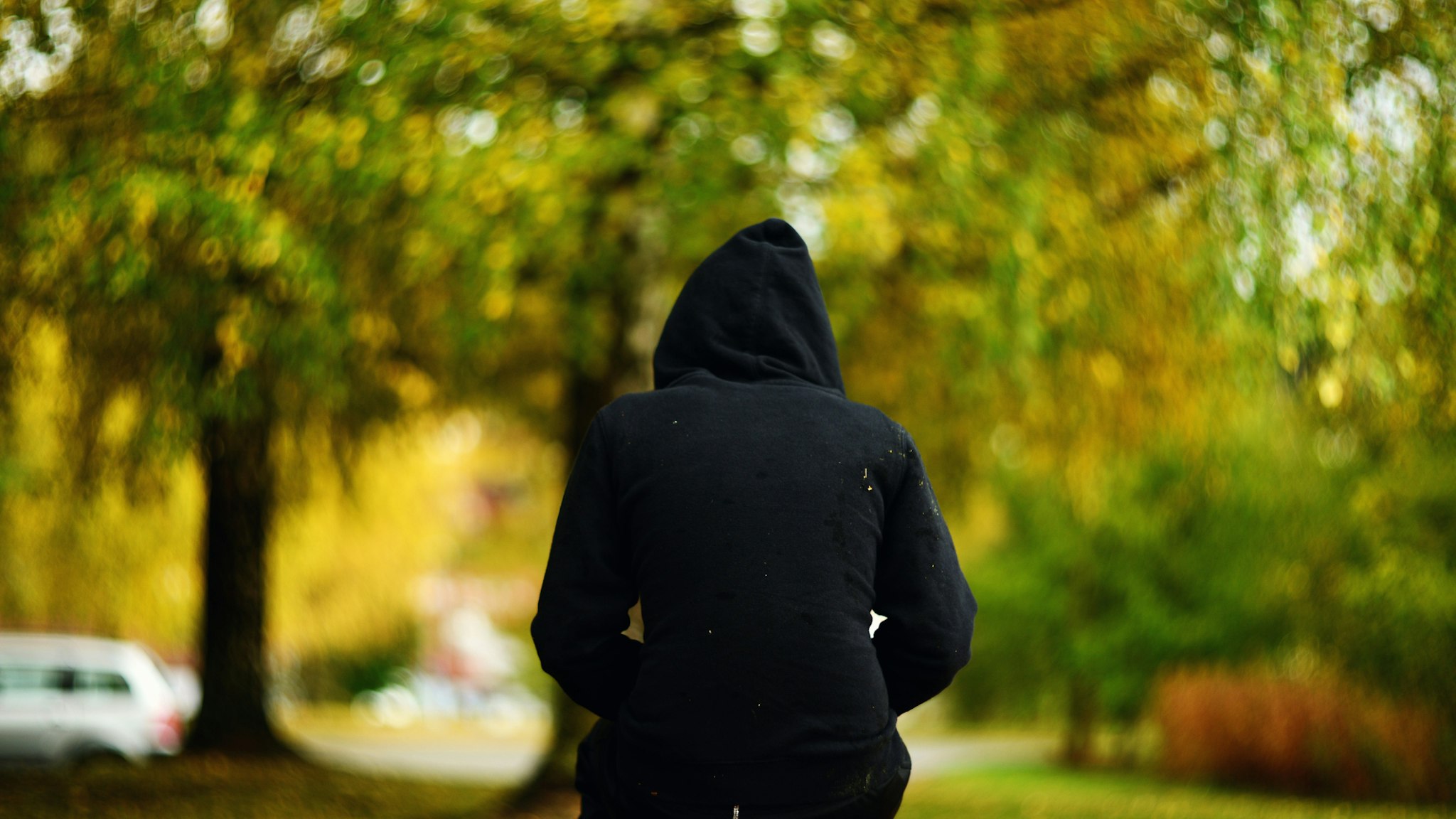 A girl in black hooded shirt with hoodie on her head sitting on a bench - stock photo
