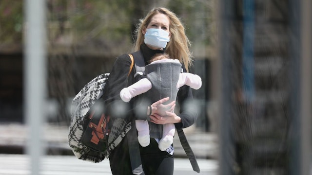 A young mother wearing a protective mask holds her baby while walking during the coronavirus pandemic on April 15, 2020 in New York City.