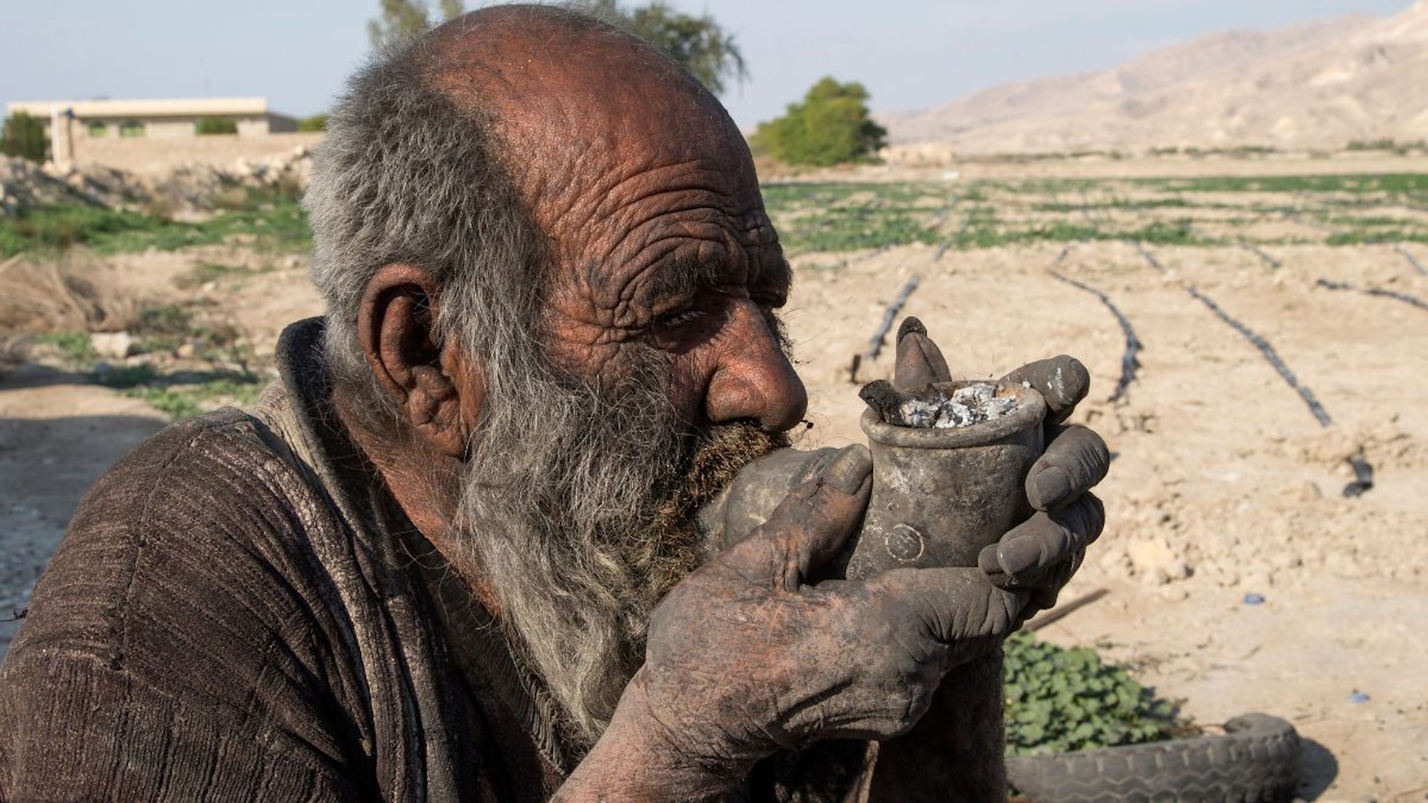 Amou Haji (uncle Haji) smokes from his waterpipe as he sits on the ground on the outskirts of the village of Dezhgah in the Dehram district of the southwestern Iranian Fars province, on December 28, 2018.