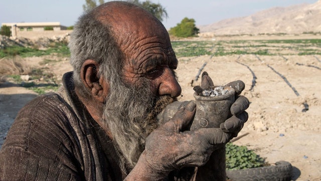 Amou Haji (uncle Haji) smokes from his waterpipe as he sits on the ground on the outskirts of the village of Dezhgah in the Dehram district of the southwestern Iranian Fars province, on December 28, 2018.
