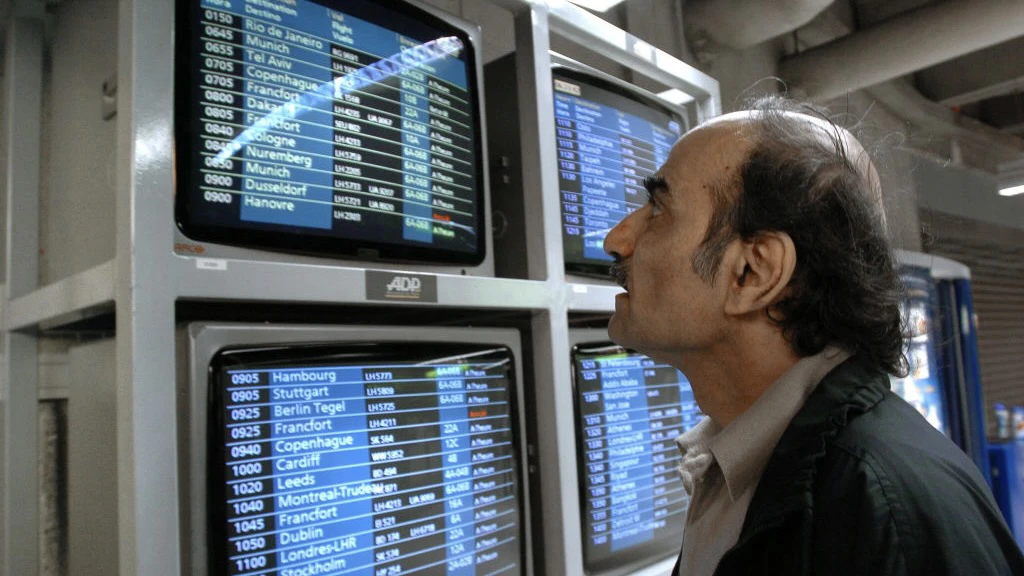 FRANCE-AIRPORT-REFUGEE-SIR ALFRED Mehran Karimi Nasseri checks the monitors 12 August 2004 in the terminal one of Paris Charles De Gaulle airport. Known as "Sir Alfred Mehran", Mehran Karimi Nasseri is a 59 year-old Iranian refugee who has been living in Roissy for 16 years, and whose life has therefore inspired American film director Steven Spielberg for the character of the protagonist in the movie "The Terminal". (Photo by STEPHANE DE SAKUTIN / AFP) (Photo by STEPHANE DE SAKUTIN/AFP via Getty Images) STEPHANE DE SAKUTIN / Contributor