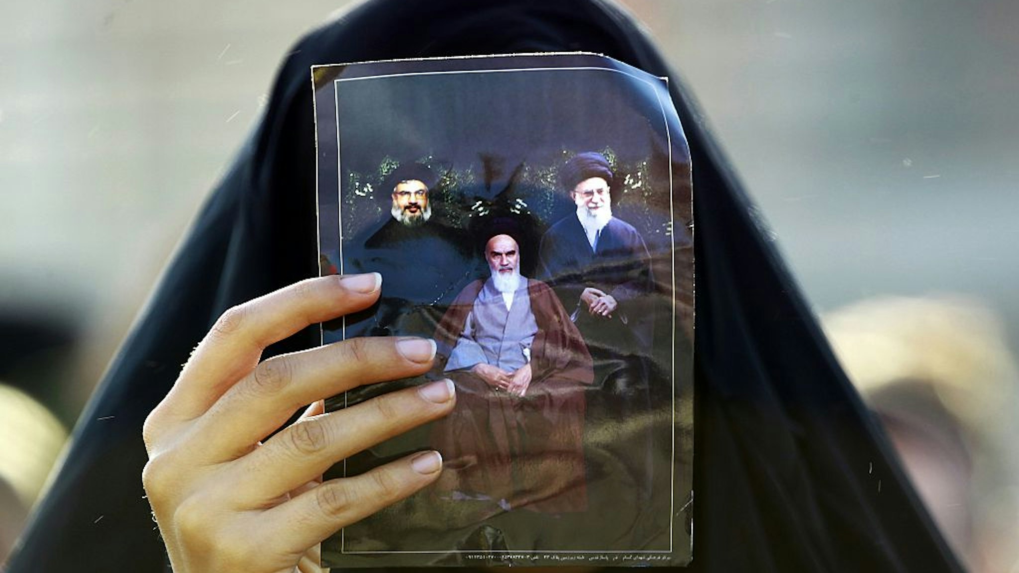 A Shiite Muslim pilgrim holds up a picture of Iranian supreme leader Ayatollah Ali Khamenei (R), Iran's late founder of the Islamic Republic Ayatollah Ruhollah Khomeini (C), and the head of Lebanon's militant Shiite Muslim movement Hezbollah, Hassan Nasrallah, during a break in Najaf on their way to the shrine central city of Karbala on December 9, 2014 where they take part in the Arbaeen religious festival which marks the 40th day after Ashura which commemorates the seventh century killing of Prophet Mohammed's grandson, Imam Hussein. In addition to the millions of Shiite devotees who flock to Karbala, some of them on foot, from across Iraq, a large contingent of Iranians traditionally make the trip. AFP PHOTO / HAIDAR HAMDANI (Photo credit should read