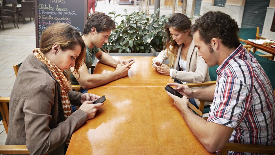 Four friends all looking at their phones at cafe Four friends all looking at their phones at cafe