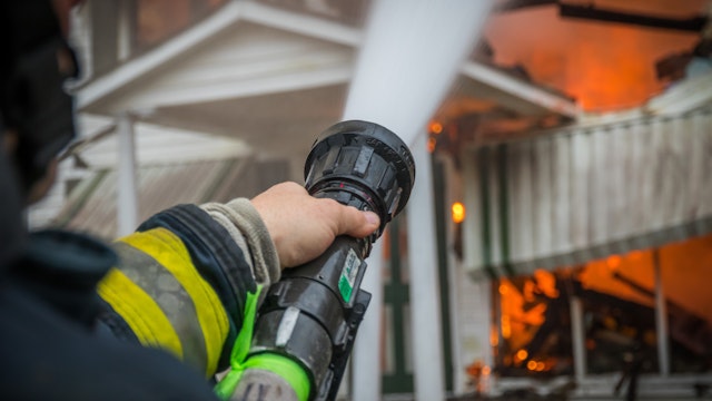 Close-Up Of A Firefighter Spraying Burning House With Hose - stock photo