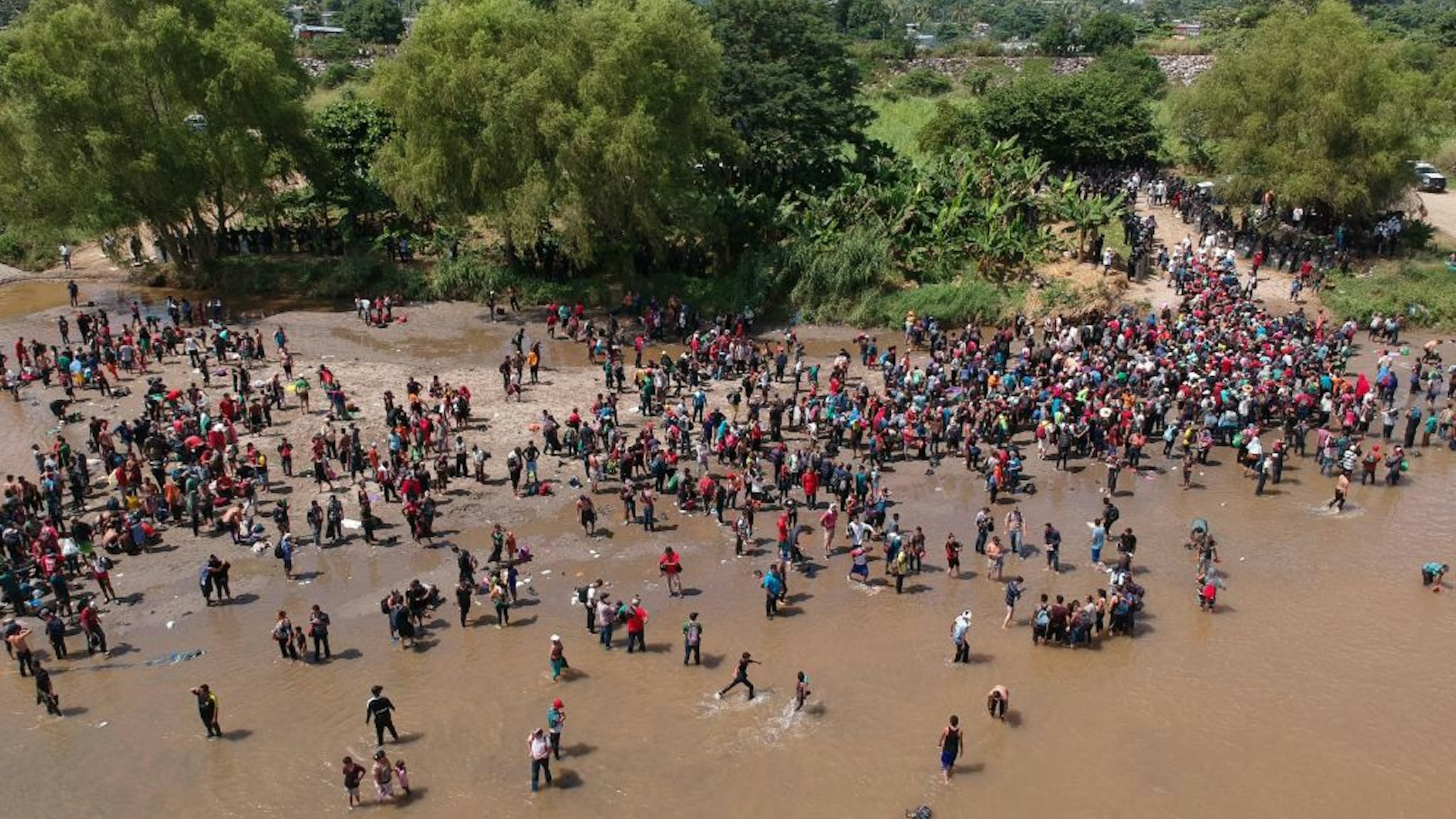TOPSHOT - Aerial view showing migrants reaching Mexico after crossing the Suchiate River from Tecun Uman in Guatemala to Ciudad Hidalgo in Mexico on October 29, 2018, a day after a security fence on the international bridge was reinforced to prevent them from passing through. - Thousands of Honduran migrants in different groups are attempting to join a larger caravan of compatriots heading towards the United States. (Photo by Carlos ALONZO / AFP) (Photo credit should read