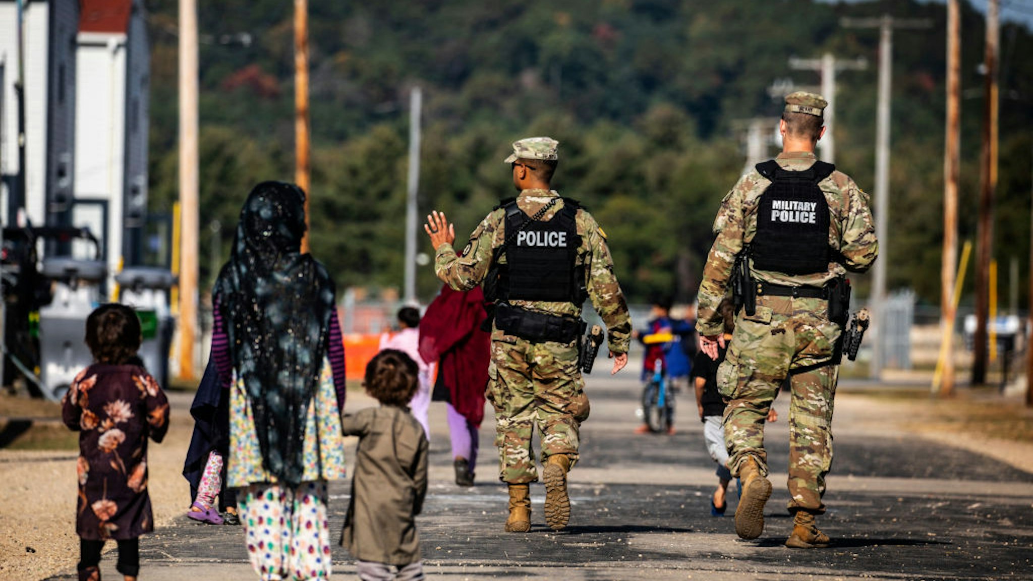 FORT MCCOY, WI - SEPTEMBER 30: U.S. Military Police walk past Afghan refugees at the Village at the Ft. McCoy U.S. Army base on September 30, 2021 in Ft. McCoy, Wisconsin. The Village is the community housing for the Afghans, comprised of eight neighborhoods where the evacuees live, eat, and receive services and support. There are approximately 12,600 Afghan refugees being cared for at the base under Operation Allies Welcome. The Department of Defense, through U.S. Northern Command and U.S. Army North, and in support of the Department of Homeland Security, is providing transportation, temporary housing, medical screening and general support for at least 50,000 Afghan evacuees at suitable facilities in permanent or temporary structures while the Afghans complete the processing necessary to resettle in the United States.