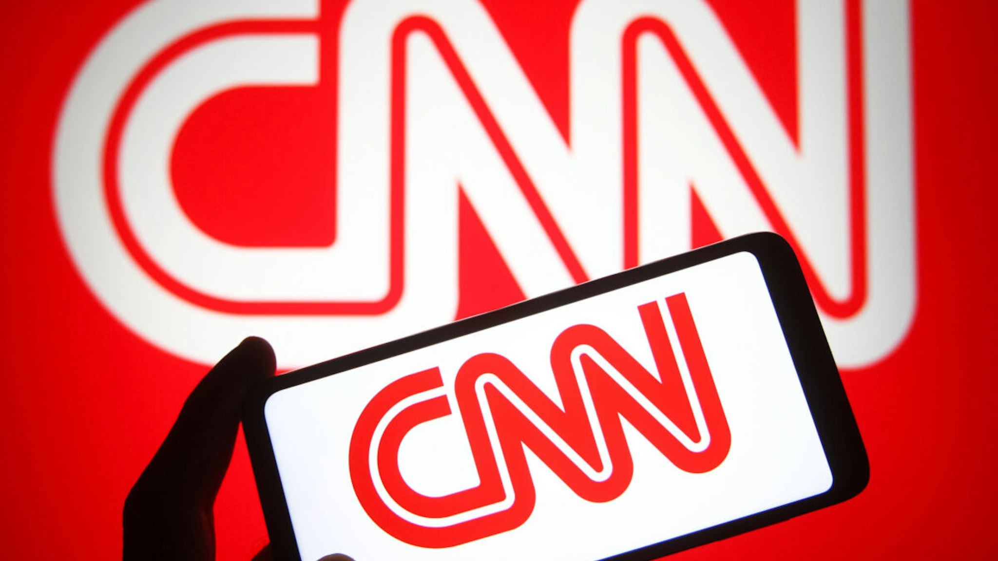 In this photo illustration a CNN (Cable News Network) logo is seen on a smartphone and a pc screen