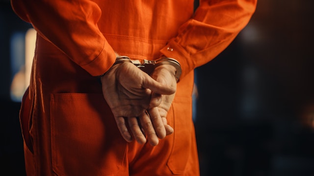 Cinematic Close Up Footage of a Handcuffed Convict at a Law and Justice Court Trial. Handcuffs on Accused Criminal in Orange Jail Jumpsuit. Law Offender Sentenced to Serve Jail Time. - stock photo