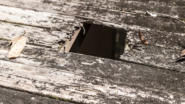 A hole in the wooden board of a 2nd floor deck, posing a hazard. Old and rotten wood planks due to exposure to weather. - stock photo