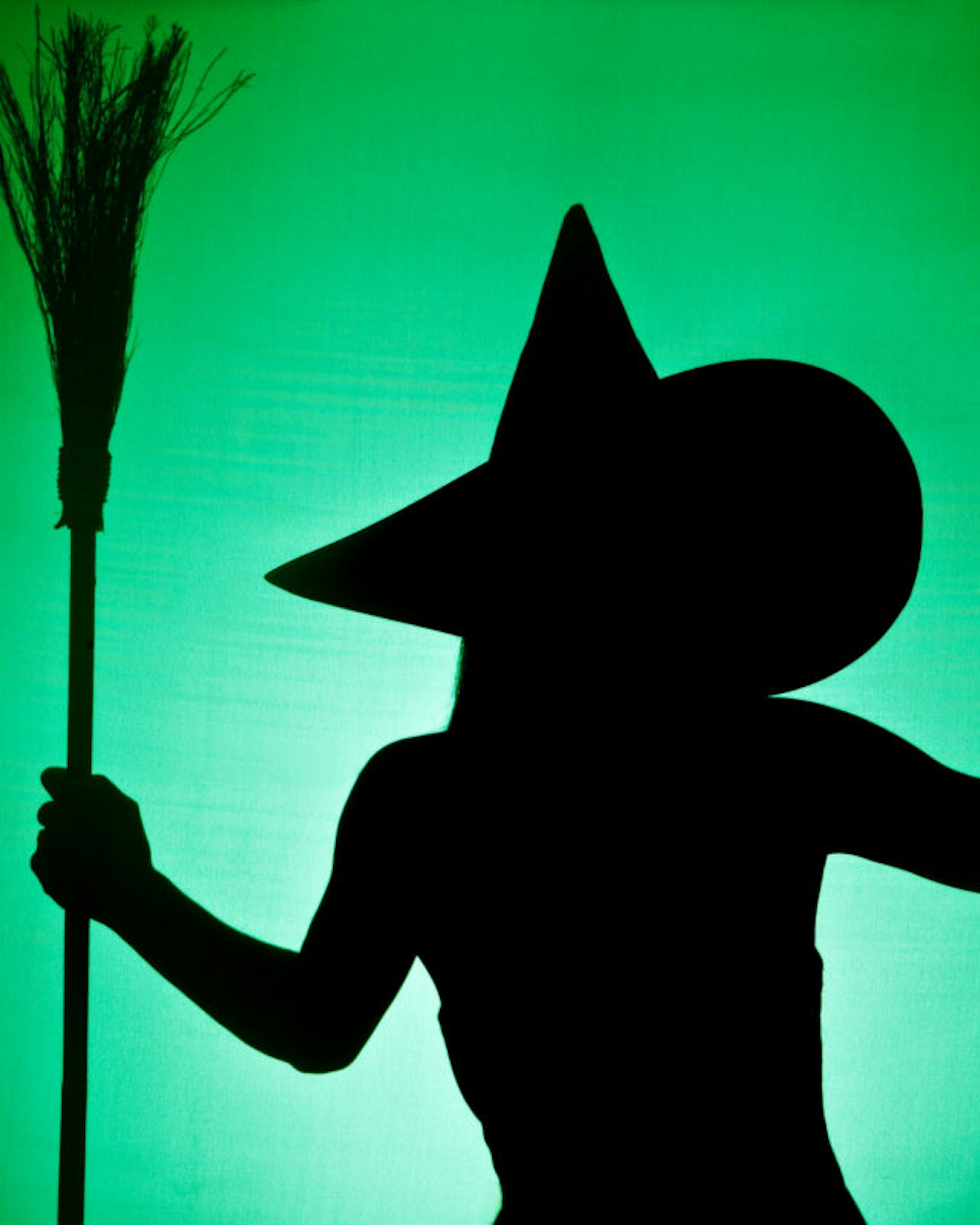 A green and black silhouette of a wicked witch holding her broom.