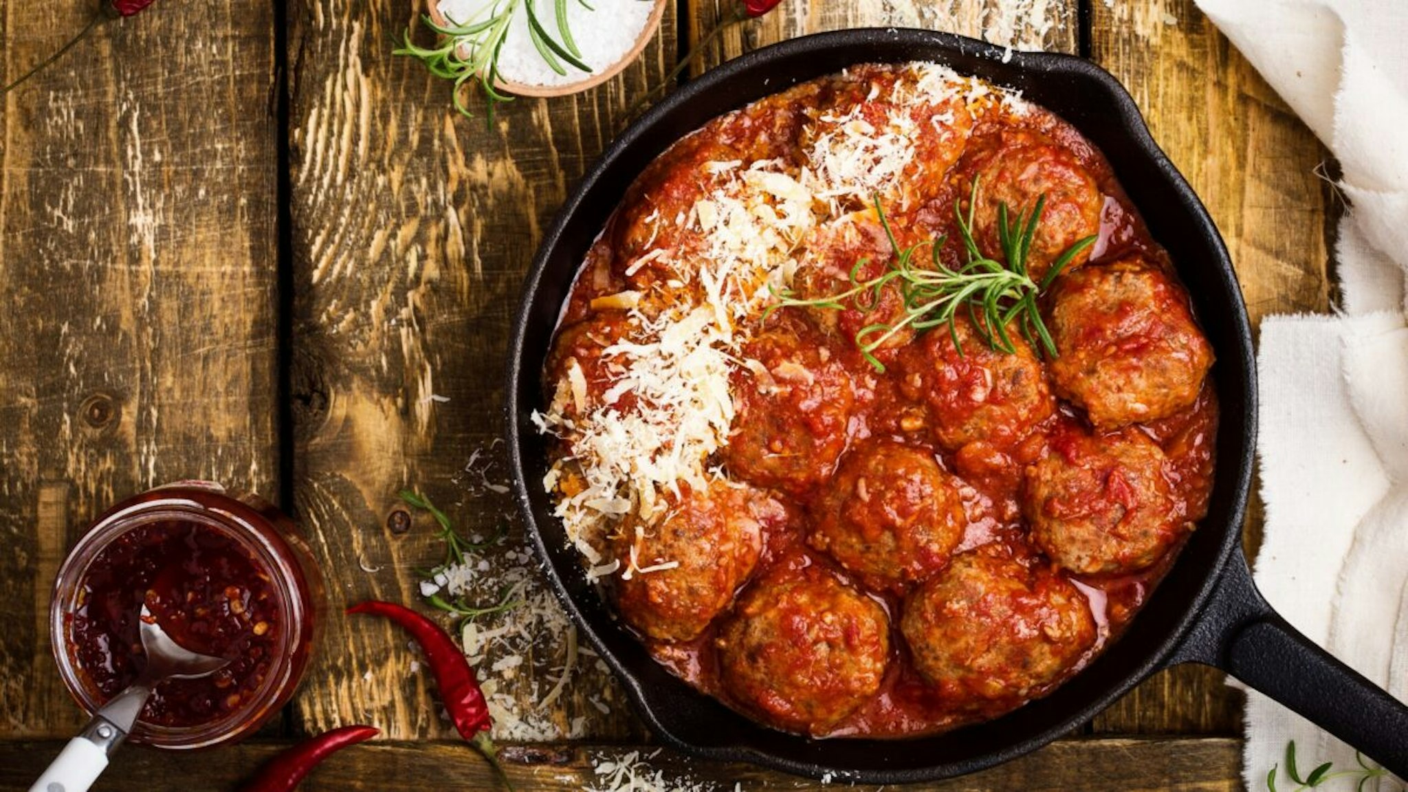 Homemade meatballs in sweet and sour tomato sauce with grated parmesan cheese on top on rustic wooden table viewed from above