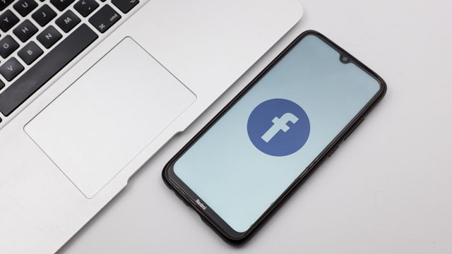 In this photo illustration a Facebook logo seen displayed on a smartphone screen on a desk next to a Macbook in Athens, Greece on November 14, 2022.
