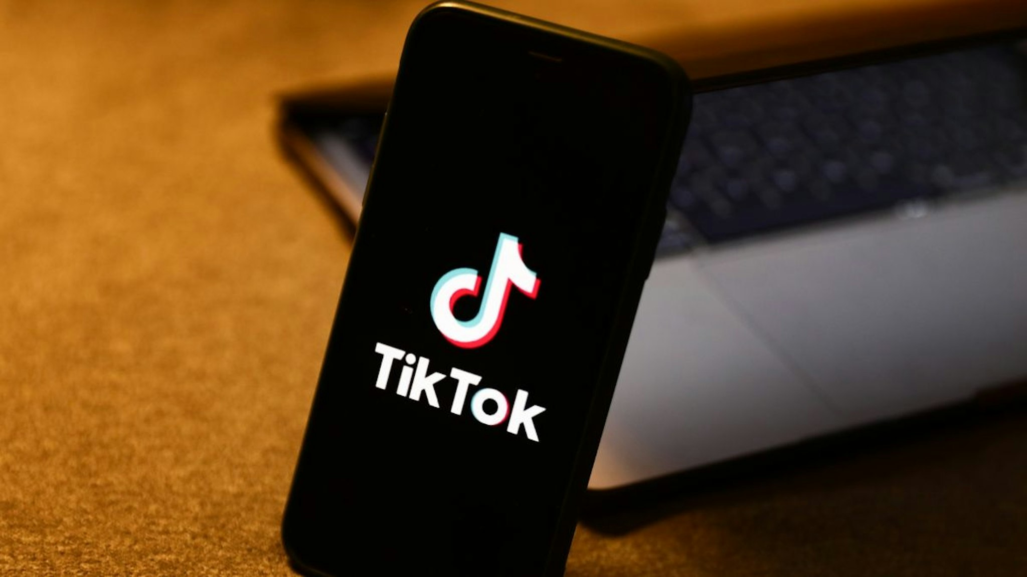 TikTok logo displayed on a phone screen and a laptop are seen in this illustration photo taken in Krakow, Poland on August 10, 2022.