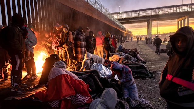 EL PASO, TEXAS - DECEMBER 22: Immigrants warm to a fire at dawn after spending the night outside next to the U.S.-Mexico border fence on December 22, 2022 in El Paso, Texas. A spike in the number of migrants seeking asylum in the United States has challenged local, state and federal authorities. The numbers are expected to increase as the fate of the Title 42 authority to expel migrants remains in limbo pending a Supreme Court decision expected after Christmas.
