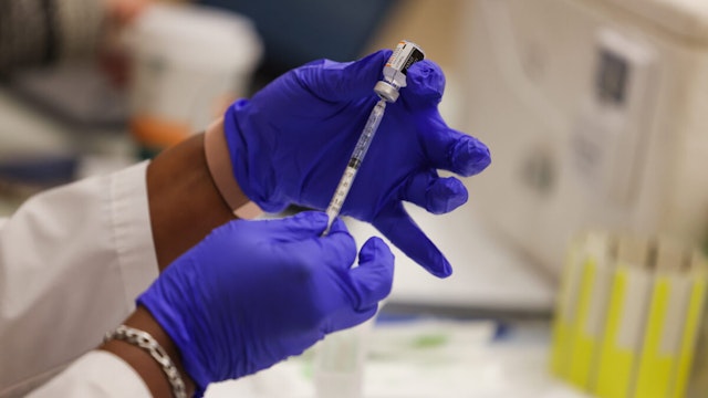 Close-up photo of gloved hands holding a Pfizer COVID-19 vaccine booster shot, administered as the Mount Sinai South Nassau Vaxmobile vists Freeport High School, in Freeport, New York on November 30, 2021