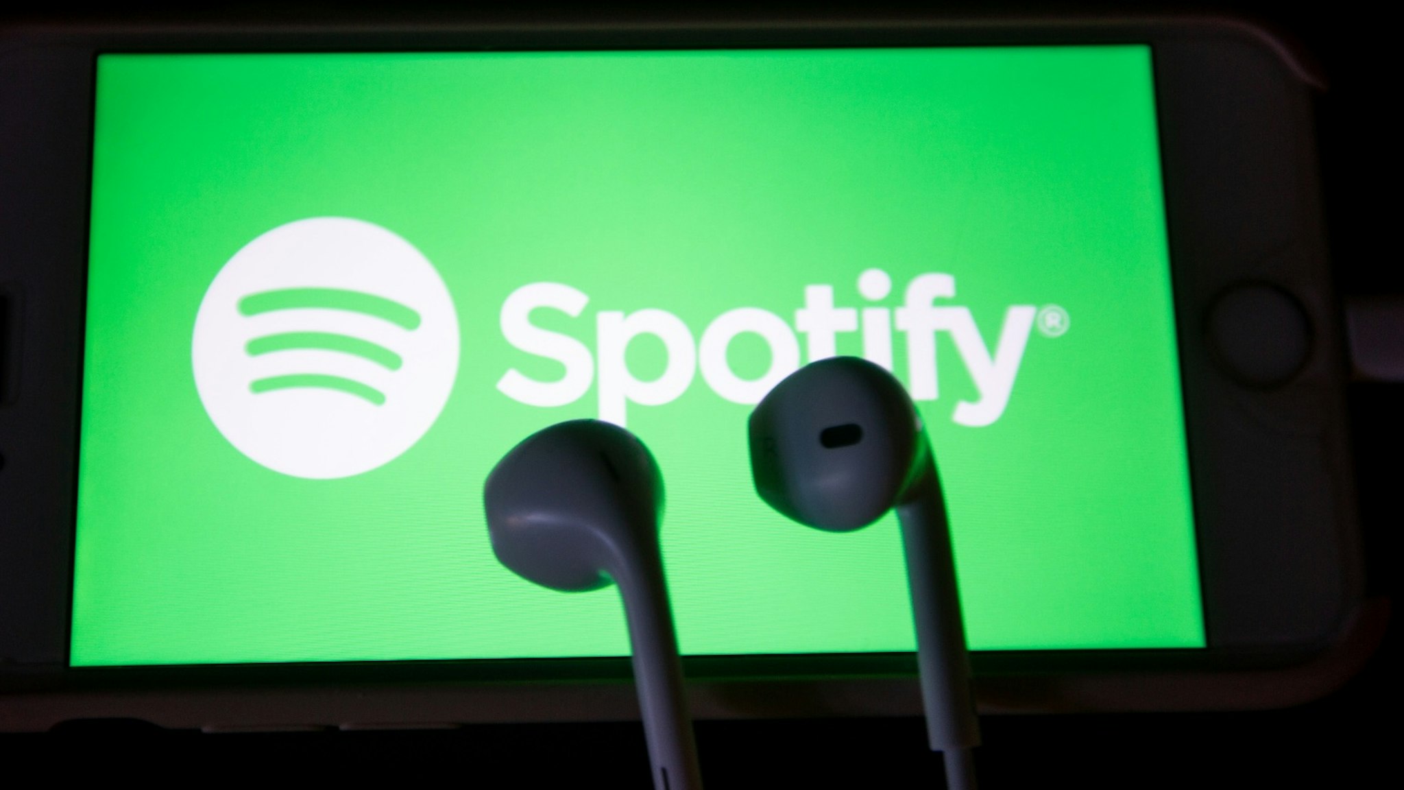 The app of the music streaming app Spotify is seen on a screen while some headphones are lying on it.