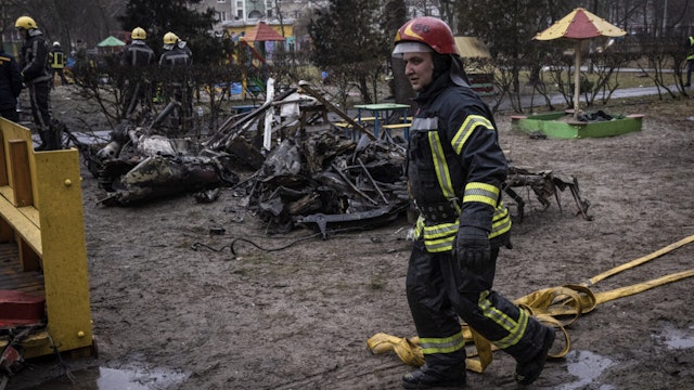 Firemen roll up hoses in front of debris as emergency service workers respond at the site of a helicopter crash on January 18, 2023 in Brovary, Ukraine