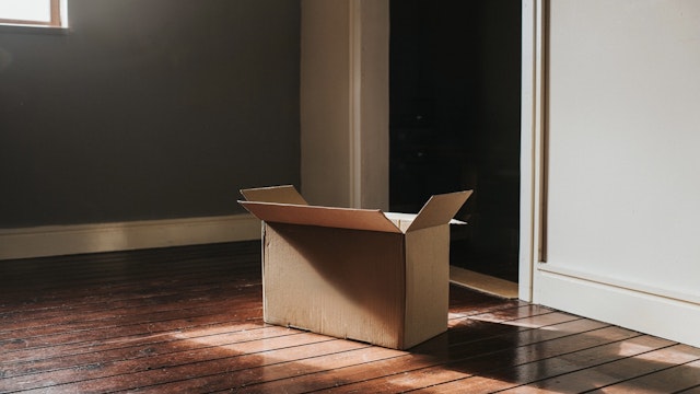 Single Cardboard Box in a Sunny Room - stock photo A single, plain, cardboard box sits on a dark wooden floor in a domestic room. Sun shines through the window creating flares and shadows. Room is empty and sparse. Wall provides a space for copy. Catherine Falls Commercial via Getty Images