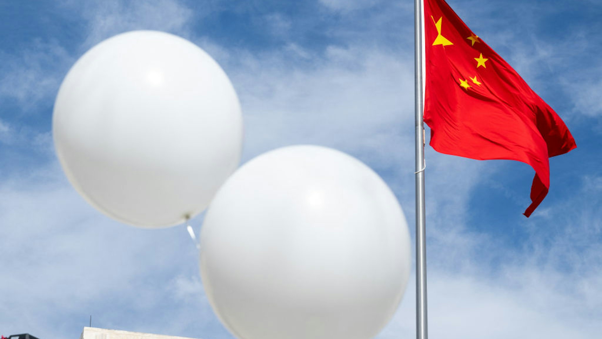 Two white balloons float near the Chinese flag as activist Rev. Patrick Mahoney protests against the Chinese government over the alleged Chinese surveillance balloon that was shot down over the US last week, during a demonstration outside the Chinese Embassy in Washington, DC, February 15, 2023. (Photo by SAUL LOEB / AFP) (Photo by SAUL