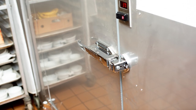 A view of a door handle that leads to a walk-in fridge inside a restaurant kitchen.