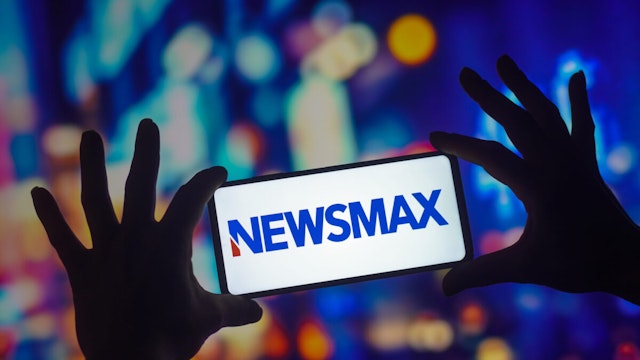 In this photo illustration, the Newsmax logo seen displayed on a smartphone