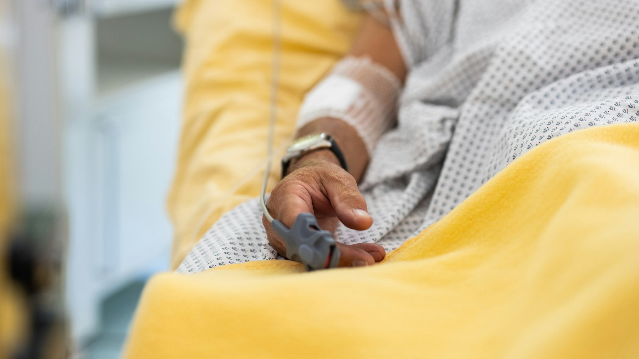 Close-up of a male patient's hand in a hospital bed with oximeter - stock photo
