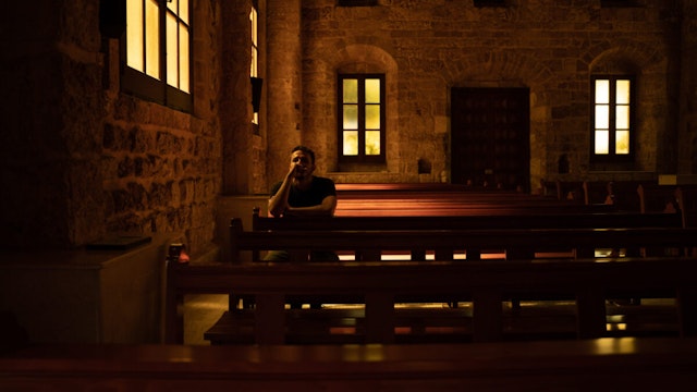 Young man is praying sitting on a bench inside of a church